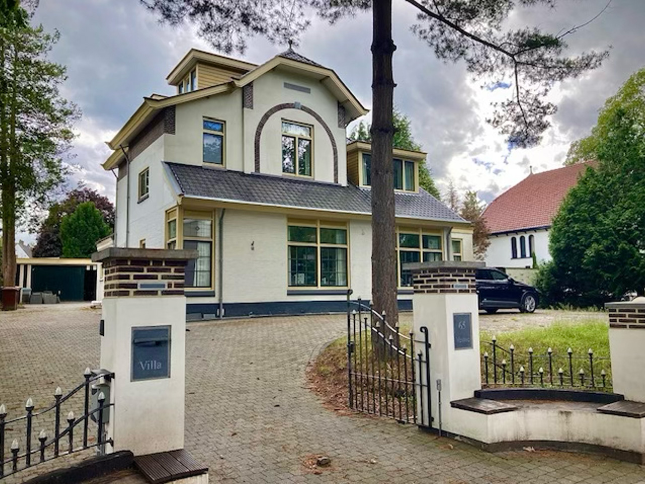 Het kantoorpand van Synvestor aan de Burg. Grothestraat 65 in Soest: een witte villa met dakkapellen, gezien vanaf het toegangshek.